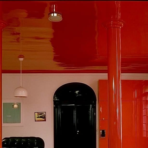 Modern room with glossy red ceiling, orange pillar, black arched door, and white pendant light.