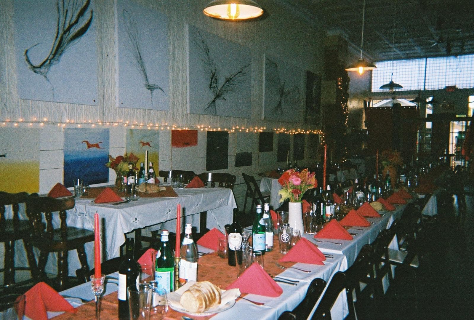 Long banquet table set with red napkins and wine bottles in an art-filled dining room.
